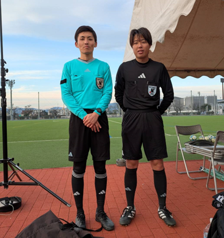 サッカーグラウンドの前に並んで立つ2人の審判員