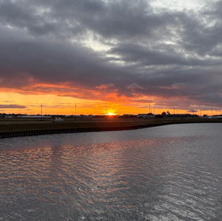 雲間からオレンジ色の夕日が覗く水辺の風景