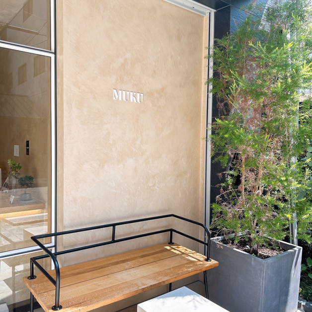 店舗「MUKU」の壁面ロゴとベンチ、観葉植物が置かれたおしゃれな外観