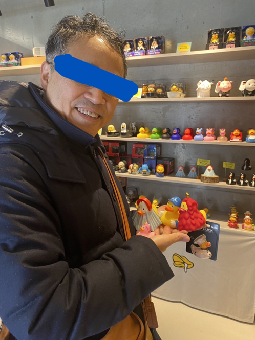 店内で複数のユニークなアヒルのおもちゃを手に載せて微笑む男性