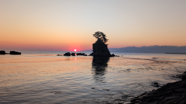 朝焼け（または夕焼け）の海に浮かぶ、松の木が生えた男岩（女岩）のシルエットと美しい水平線