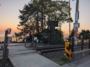 線路の向こうに鳥居と海が見える、夕暮れ時の踏切風景