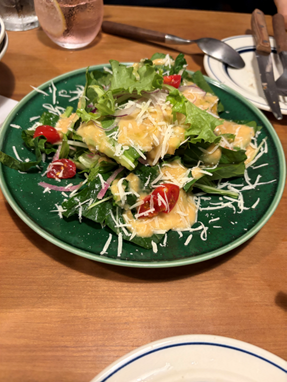 粉チーズとドレッシングがかかった、フレッシュな葉物野菜とトマトのサラダ