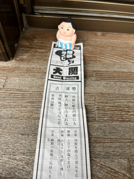 「大関」と書かれた相撲みくじの結果の上にちょこんと乗る、愛らしいお相撲さんのミニフィギュア